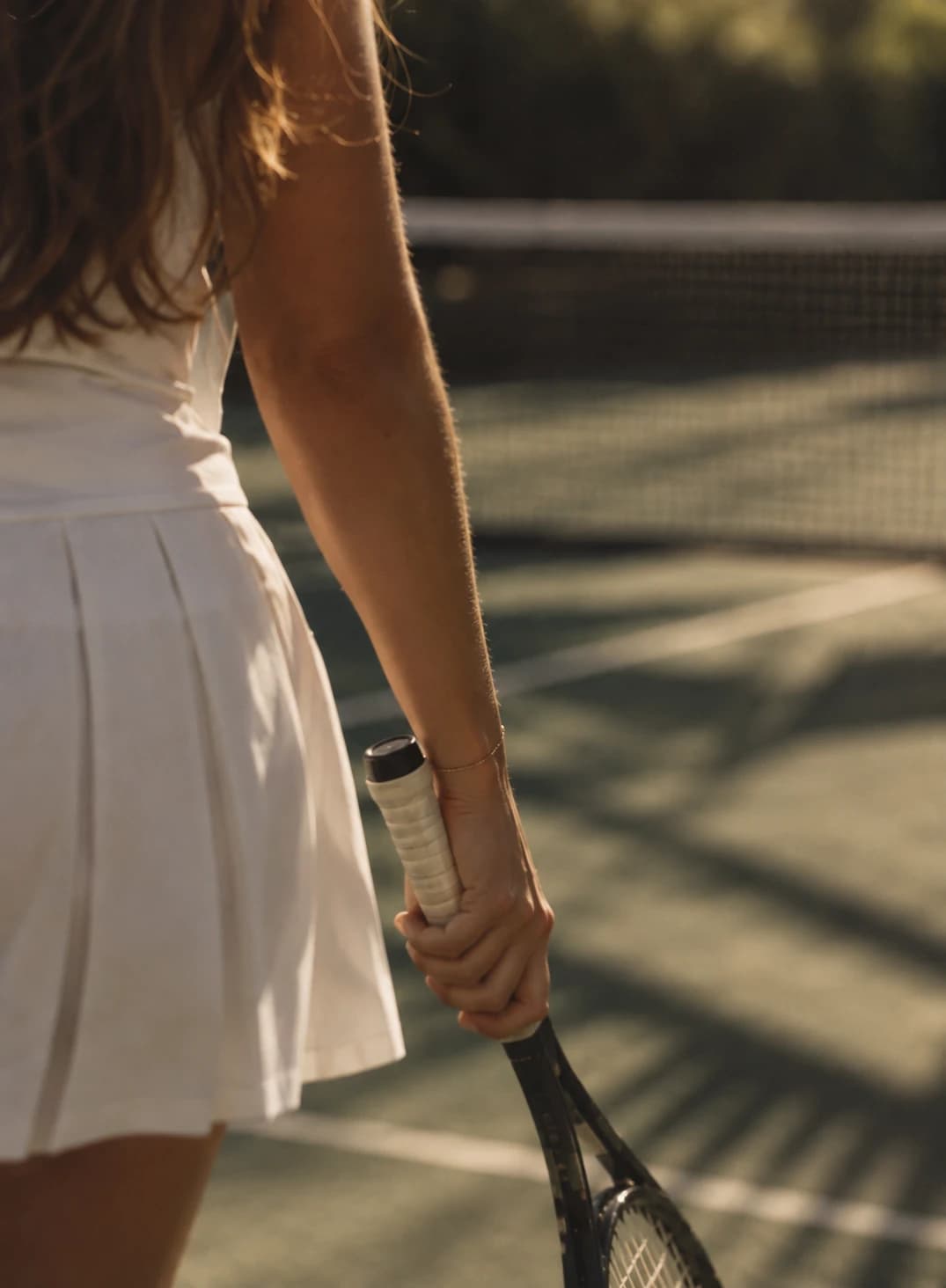 A tennis player holding a racket at her side in warm afternoon light